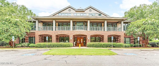 view of front of house with uncovered parking, brick siding, and a balcony