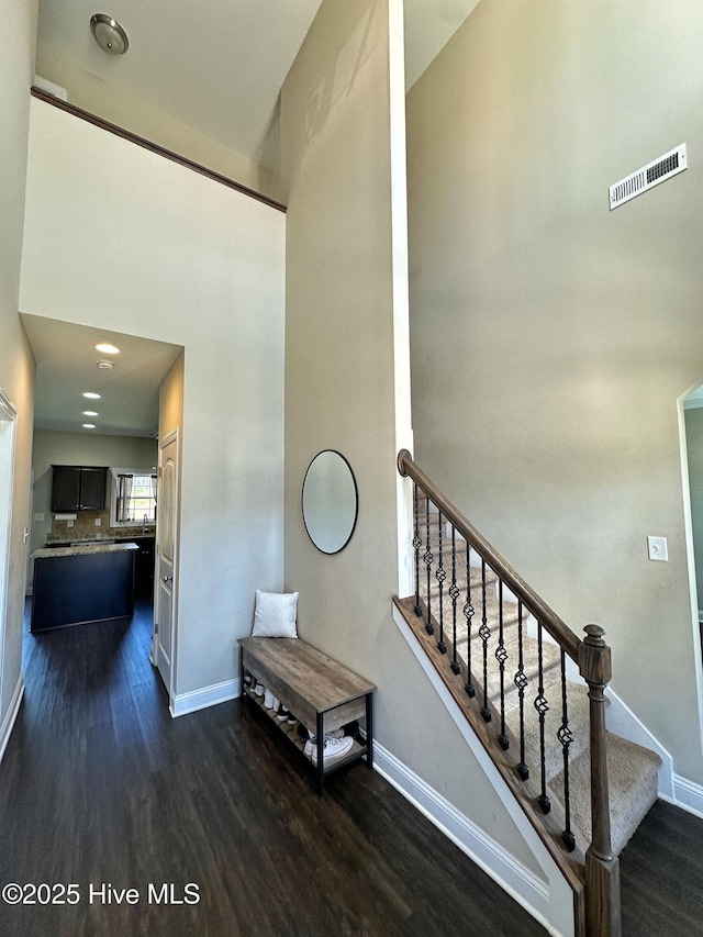 stairs featuring wood finished floors, visible vents, a high ceiling, and baseboards
