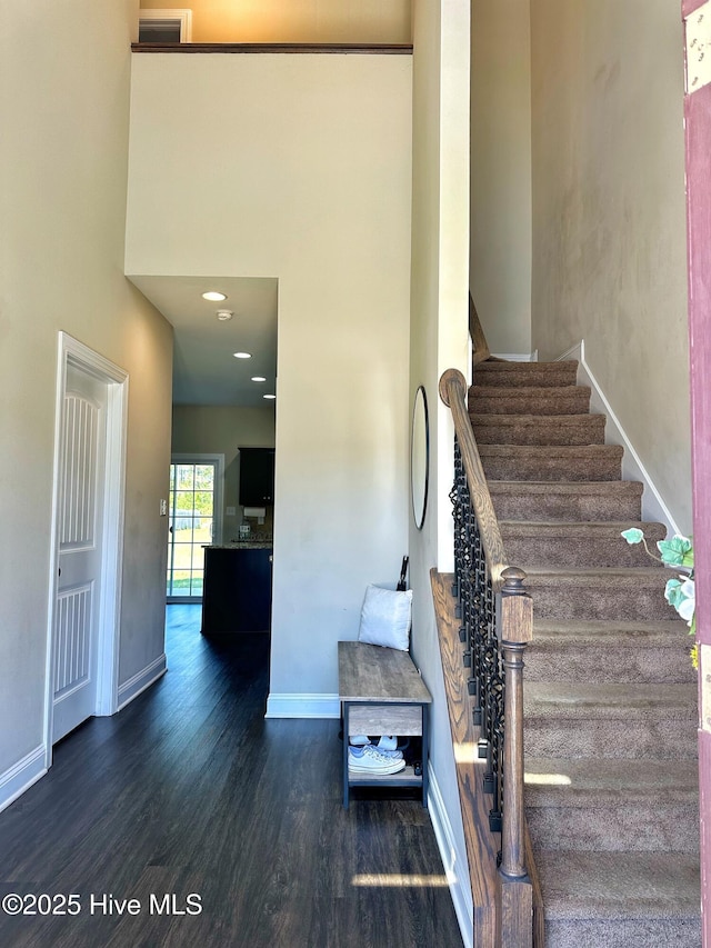 stairway featuring wood finished floors, a high ceiling, visible vents, and baseboards