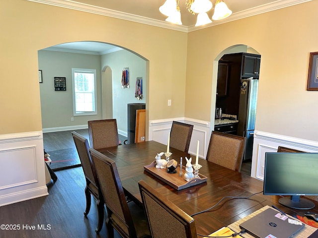 dining area with arched walkways, a notable chandelier, ornamental molding, and dark wood-style flooring