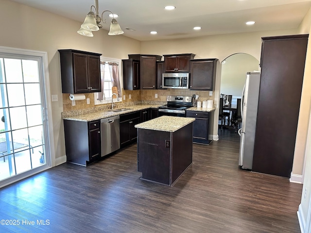 kitchen featuring a sink, stainless steel appliances, decorative backsplash, a kitchen island, and dark wood finished floors