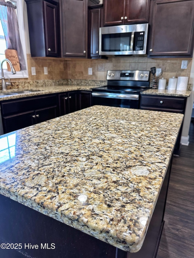 kitchen featuring tasteful backsplash, a sink, stainless steel appliances, dark wood-style floors, and light stone countertops