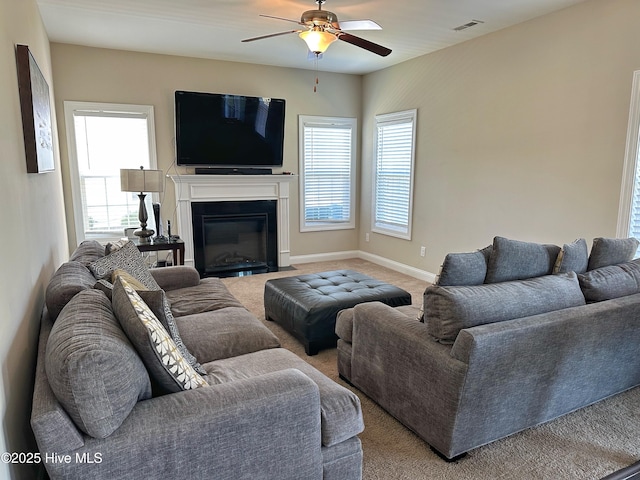 living room with light carpet, a glass covered fireplace, baseboards, visible vents, and a ceiling fan