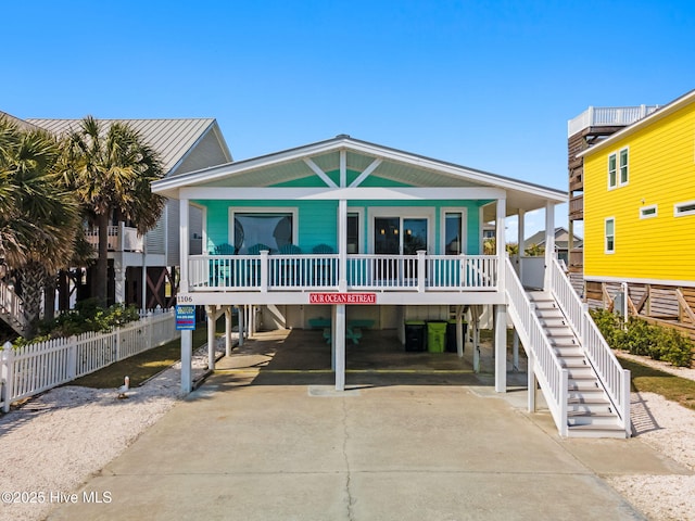 coastal home featuring a porch, driveway, stairway, and a carport
