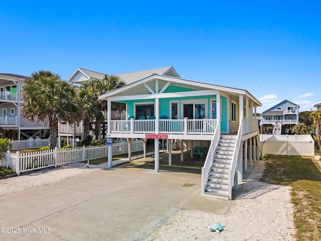 coastal home featuring fence, a carport, concrete driveway, and stairs