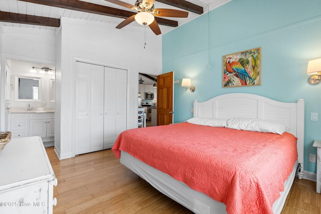 bedroom featuring light wood finished floors, a sink, a closet, ceiling fan, and vaulted ceiling with beams