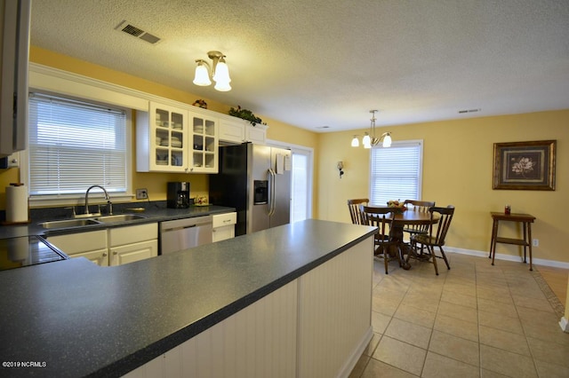 kitchen featuring visible vents, appliances with stainless steel finishes, dark countertops, a sink, and a notable chandelier