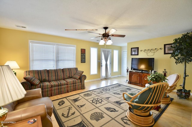 living area with baseboards, a ceiling fan, wood finished floors, and visible vents
