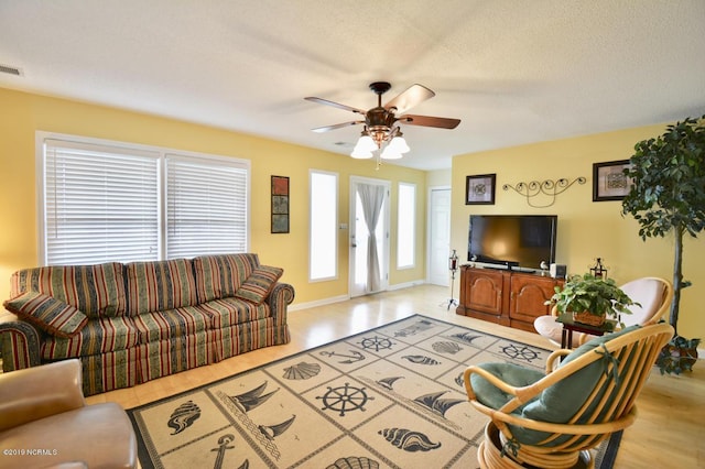 living area featuring baseboards, a ceiling fan, light wood-style flooring, and visible vents