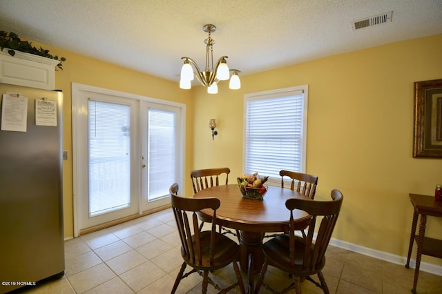 dining area with an inviting chandelier, a textured ceiling, french doors, light tile patterned floors, and visible vents