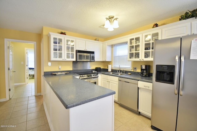 kitchen featuring dark countertops, white cabinets, a sink, light tile patterned floors, and stainless steel appliances