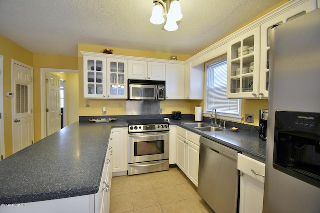 kitchen with light tile patterned flooring, dark countertops, a sink, a notable chandelier, and stainless steel appliances
