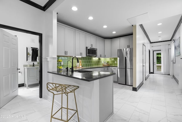 kitchen featuring a sink, marble finish floor, a peninsula, dark countertops, and appliances with stainless steel finishes