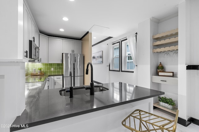 kitchen featuring a sink, tasteful backsplash, a peninsula, dark countertops, and appliances with stainless steel finishes
