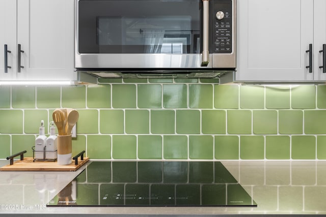 interior details featuring stainless steel microwave, white cabinetry, and backsplash