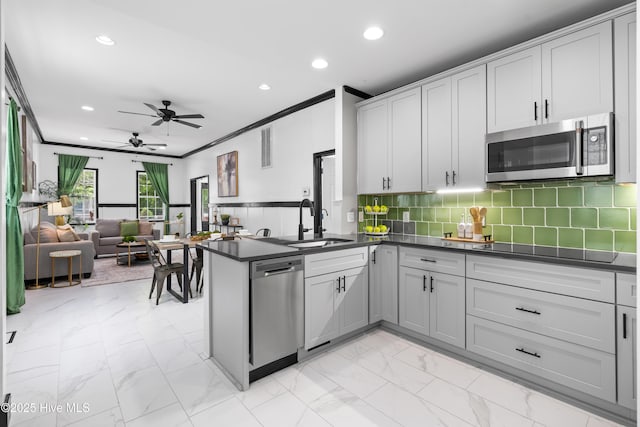 kitchen with a sink, marble finish floor, a peninsula, dark countertops, and appliances with stainless steel finishes