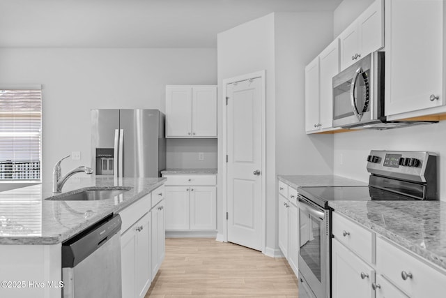 kitchen featuring a sink, white cabinets, stainless steel appliances, light wood-style flooring, and an island with sink