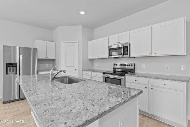 kitchen featuring appliances with stainless steel finishes, a sink, light stone counters, white cabinetry, and an island with sink