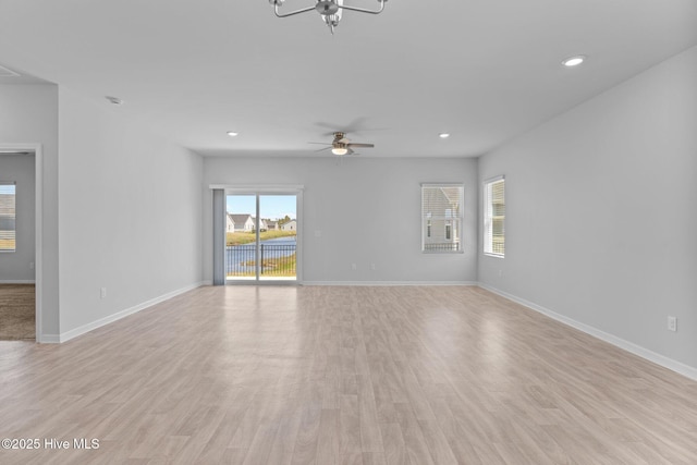 unfurnished living room with baseboards, ceiling fan with notable chandelier, recessed lighting, and light wood-style flooring
