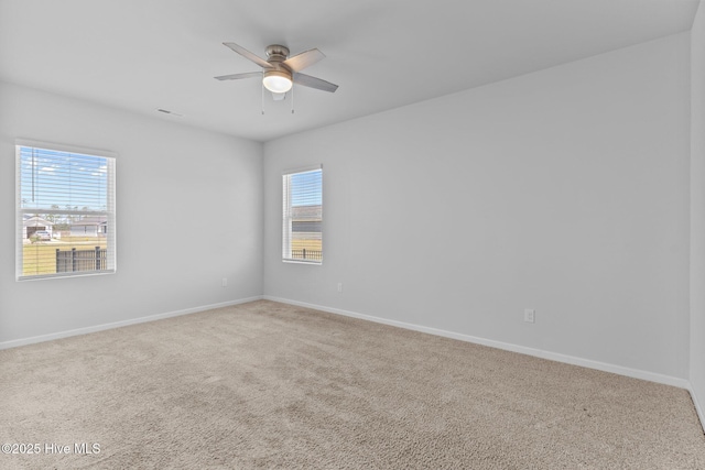 unfurnished room with carpet floors, a ceiling fan, baseboards, and a wealth of natural light