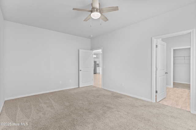 unfurnished bedroom with freestanding refrigerator, baseboards, a spacious closet, a ceiling fan, and carpet