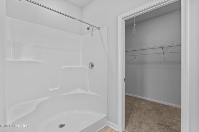 full bathroom with baseboards, a shower, and a walk in closet