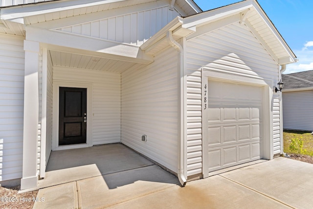 view of exterior entry featuring an attached garage, board and batten siding, and concrete driveway