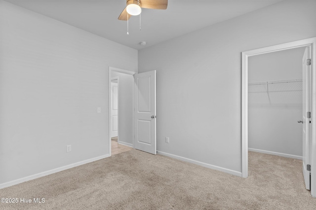 unfurnished bedroom with a walk in closet, ceiling fan, baseboards, a closet, and carpet flooring