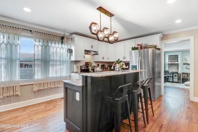 kitchen featuring light wood-type flooring, under cabinet range hood, stainless steel fridge, and baseboards