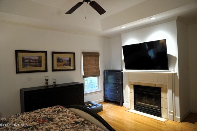 bedroom featuring a raised ceiling, a fireplace, recessed lighting, baseboards, and wood finished floors