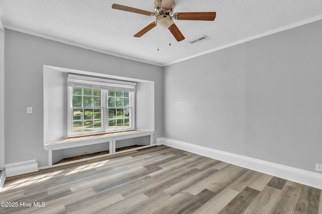 spare room with visible vents, baseboards, ornamental molding, wood finished floors, and a ceiling fan