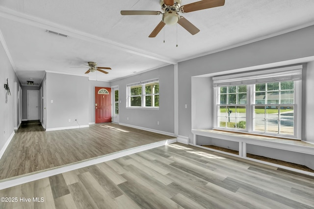 unfurnished living room featuring wood finished floors, ornamental molding, ceiling fan, baseboards, and visible vents