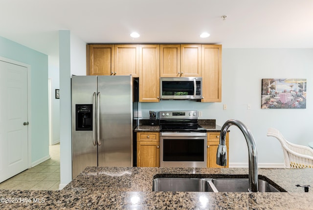 kitchen featuring recessed lighting, dark stone counters, appliances with stainless steel finishes, a sink, and light tile patterned flooring