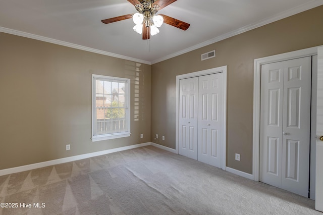 unfurnished bedroom featuring crown molding, light carpet, multiple closets, baseboards, and visible vents