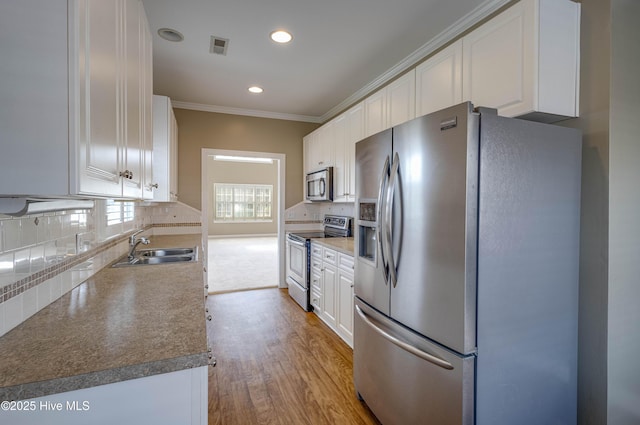 kitchen with light wood-type flooring, white cabinetry, tasteful backsplash, a sink, and appliances with stainless steel finishes