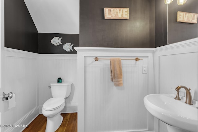 bathroom with a sink, wood finished floors, wainscoting, toilet, and a decorative wall