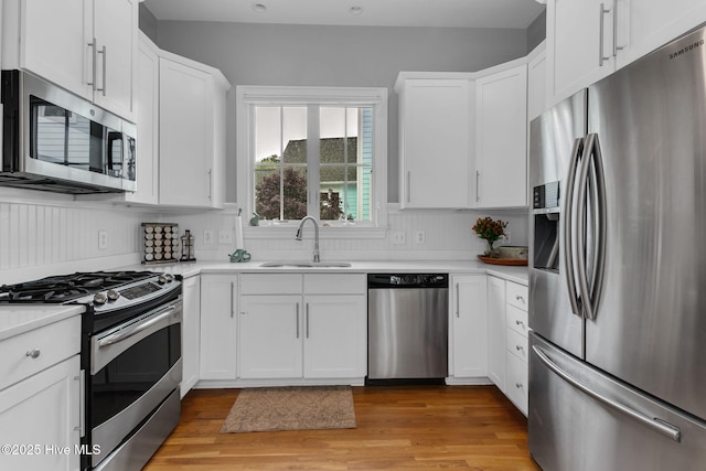 kitchen with stainless steel appliances, a sink, white cabinets, light countertops, and light wood-type flooring