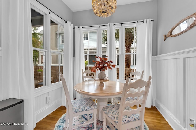 dining area featuring wood finished floors, a decorative wall, a wainscoted wall, and a chandelier