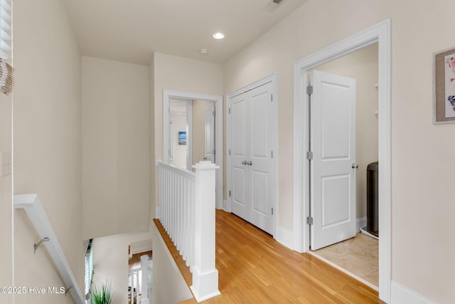hall with an upstairs landing, light wood finished floors, and recessed lighting