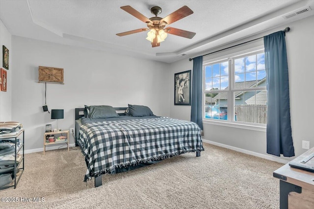 carpeted bedroom featuring visible vents, a ceiling fan, baseboards, and a tray ceiling