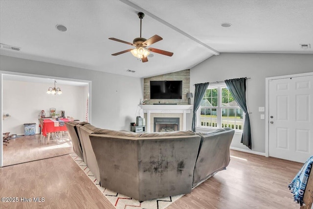 living area featuring visible vents, a large fireplace, ceiling fan with notable chandelier, light wood finished floors, and vaulted ceiling with beams