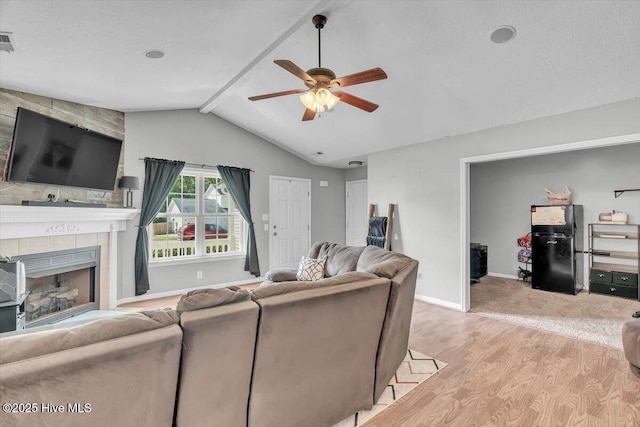 living room featuring baseboards, vaulted ceiling with beams, a tiled fireplace, a ceiling fan, and light wood-style flooring