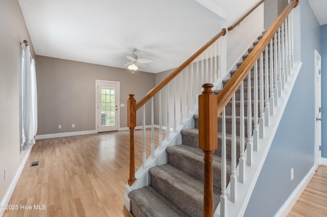 stairs with a ceiling fan, visible vents, wood finished floors, and baseboards