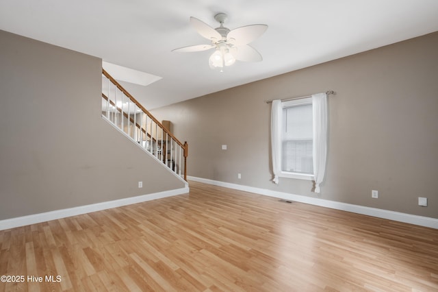 unfurnished living room featuring light wood-style floors, baseboards, ceiling fan, and stairs