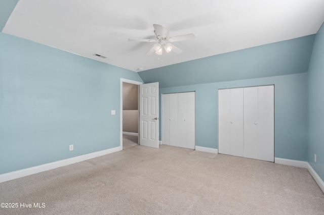 unfurnished bedroom featuring two closets, carpet, vaulted ceiling, baseboards, and visible vents