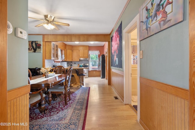 dining space featuring light wood finished floors, wooden walls, a ceiling fan, visible vents, and wainscoting