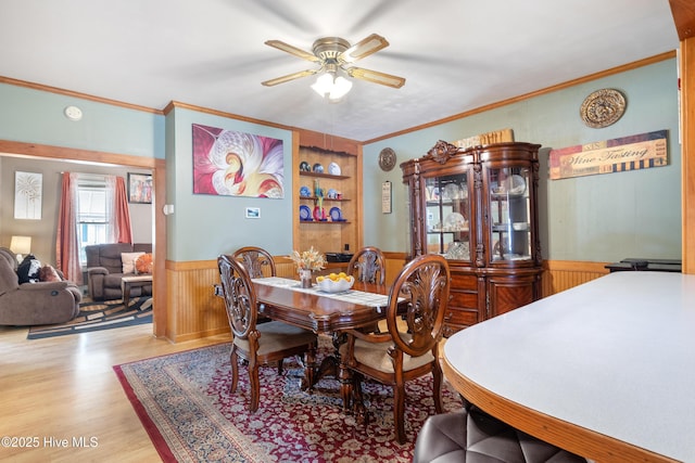 dining area with crown molding, a ceiling fan, wainscoting, and wood finished floors