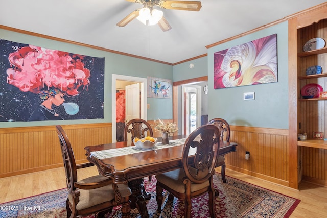 dining room with crown molding, a wainscoted wall, wooden walls, wood finished floors, and a ceiling fan