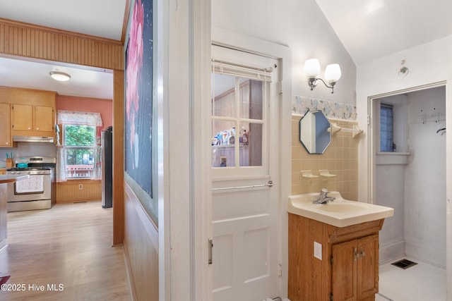 bathroom with vanity, tile walls, vaulted ceiling, and wood finished floors