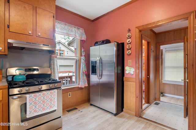 kitchen with stainless steel appliances, light wood-style floors, under cabinet range hood, ornamental molding, and wooden walls